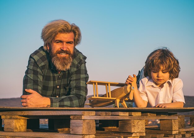 Glücklicher Vater und Sohn auf der Wiese im Sommer. Kindervater und -sohn-Fantasiepilotflieger mit Flugzeugträumen vom Reisen.