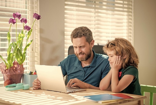 Glücklicher Vater und Sohn in der Schule, die online an Laptop-Online-Bildung arbeiten