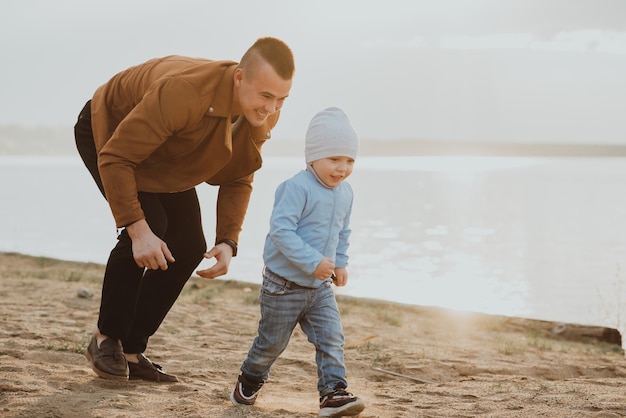 Glücklicher Vater und Sohn spielen im Sommer auf dem Sand am Strand am Fluss