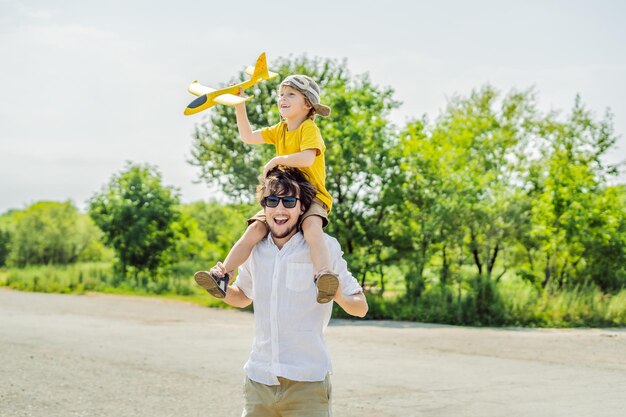 Glücklicher Vater und Sohn spielen mit Spielzeugflugzeug vor altem Start- und Landebahnhintergrund Reisen mit Kinderkonzept