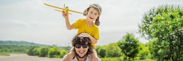 Glücklicher Vater und Sohn spielen mit Spielzeugflugzeug vor dem Hintergrund der alten Landebahn und reisen mit Kindern
