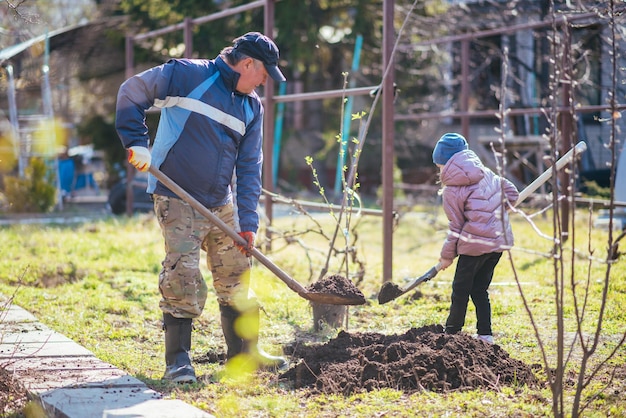 Glücklicher Vater und Tochter, die im Frühjahr einen neuen Baum im Dorf pflanzen