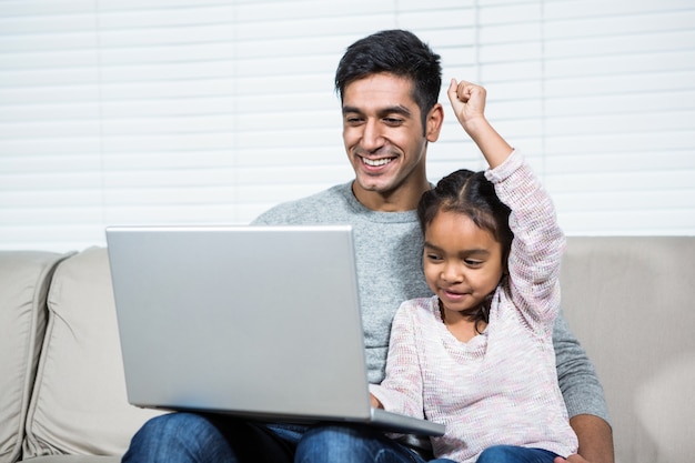 Glücklicher Vater und Tochter, die Laptop auf dem Sofa verwendet