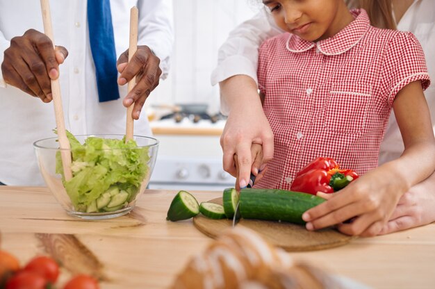 Glücklicher Vater und Tochter kochen Salat zum Frühstück. Lächelnde Familie isst morgens in der Küche. Papa füttert weibliches Kind, gute Beziehung