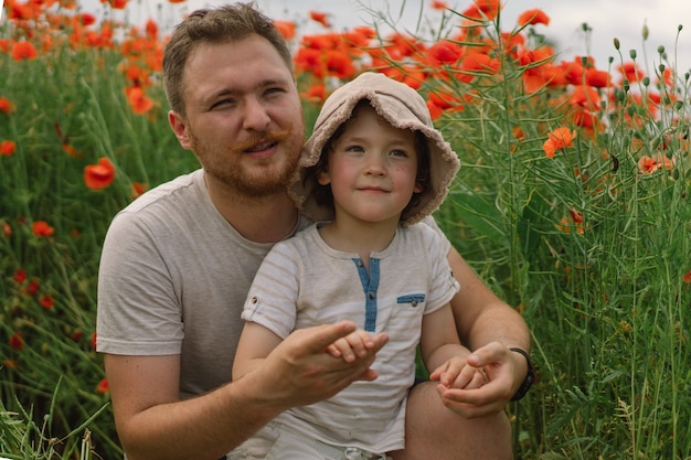 Glücklicher Vatertag kleiner Junge und Vater spielen in einem schönen Feld mit roten Mohnblumen