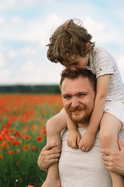 Glücklicher Vatertag kleiner Junge und Vater spielen in einem schönen Feld mit roten Mohnblumen