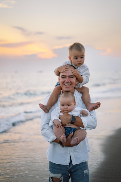 Glücklicher Vatertag Vater und Kinder spielen am Strand Vater und er Childs genießen zusammen den Sonnenuntergang Liebevoller alleinerziehender Vater umarmt niedlichen kleinen zwei Sohn