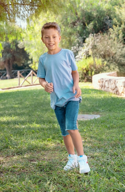 Glücklicher Vorschulkindjunge, der am sonnigen Tag in einem Park im Freien läuft. Nettes Kind mit Hemd und Jeans-Shorts, das Sport treibt und Spaß hat. Aktive Hobbys, gesundes Lifestyle-Konzept. T-Shirt-Modell