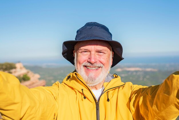 Glücklicher Wanderer im Ruhestand, der mit seinem Smartphone ein Selfie macht, das einen Berg erwandert