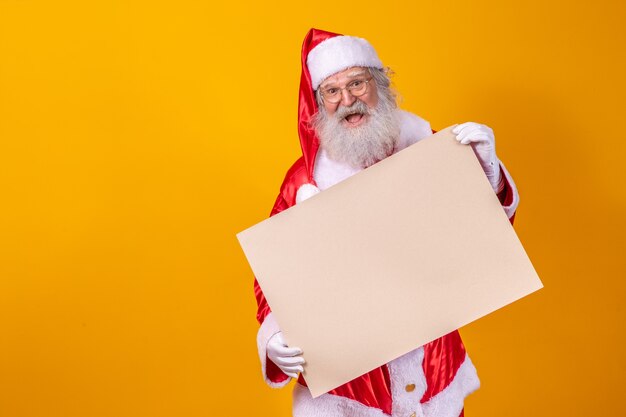 Glücklicher Weihnachtsmann, der ein leeres Brett lokalisiert auf gelbem Hintergrund mit Kopienraum hält.