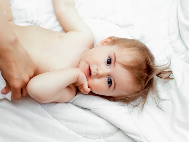Glückliches 11 Monate altes Baby, das auf einer weißen Decke liegt und lächelt