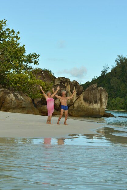 Glückliches älteres Ehepaar ruht sich am tropischen Strand mit den Händen hoch aus