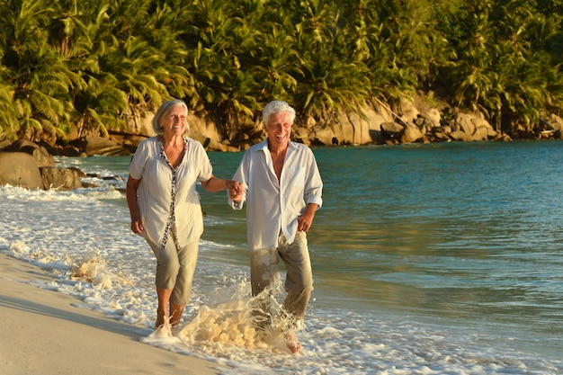 Glückliches älteres Ehepaar ruht sich bei Sonnenuntergang am tropischen Strand aus