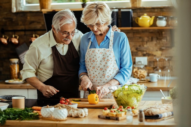 Glückliches älteres Paar, das beim gemeinsamen Kochen in der Küche eine gesunde Mahlzeit zubereitet.