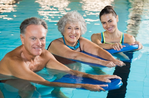 Glückliches älteres Paar, das Schwimmunterricht vom jungen Trainer nimmt