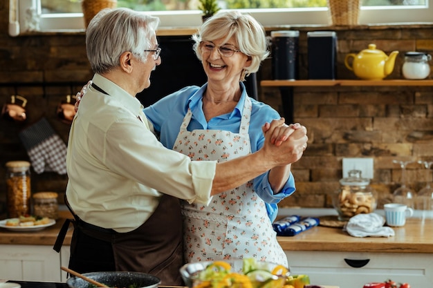 Glückliches älteres Paar, das Spaß hat und tanzt, während es in der Küche kocht