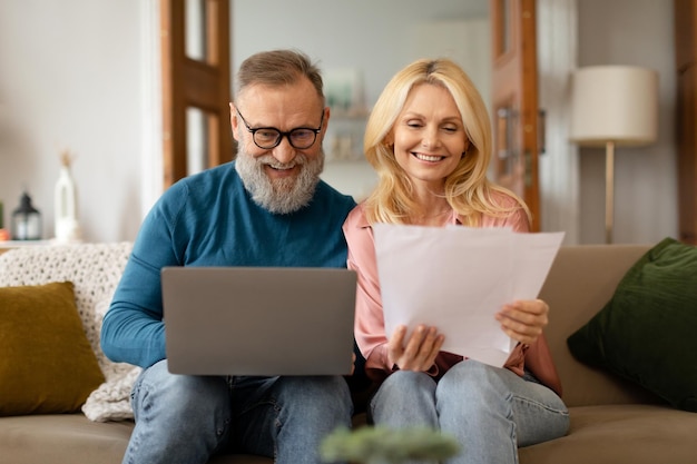 Glückliches älteres Paar, das zu Hause Papierkram erledigt und einen Laptop benutzt