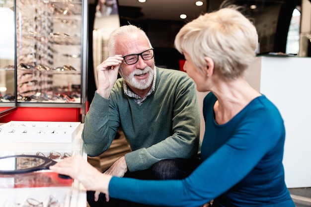 Glückliches älteres Paar, das zusammen Brillenrahmen im Optikgeschäft wählt.