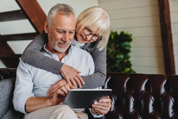 Glückliches älteres Paar mit digitalem Tablet im Wohnzimmer