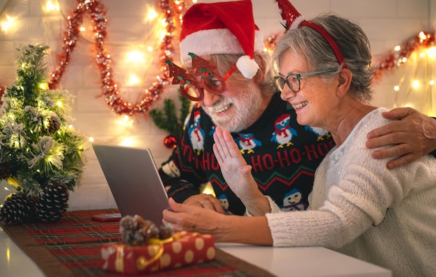 Glückliches älteres Paar mit Weihnachtsmütze zur Weihnachtszeit im Videoanruf per Laptop von zu Hause aus, um mit Familie oder Freunden in Kontakt zu treten