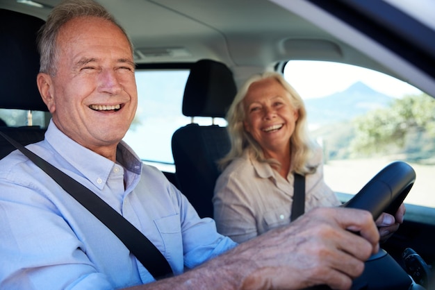 Glückliches älteres weißes Paar, das in ihrem Auto fährt und zur Kameraseitenansicht aus der Nähe lächelt