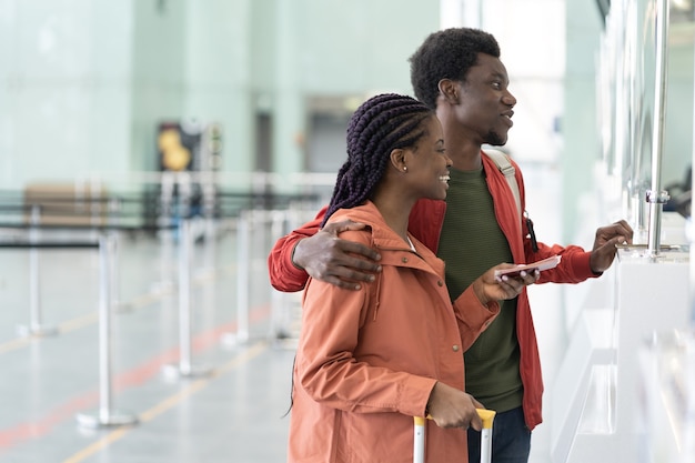 Glückliches afrikanisches Paar mit ausländischen Pässen und Bordkarten, die am Check-in-Schalter des Flughafens stehen