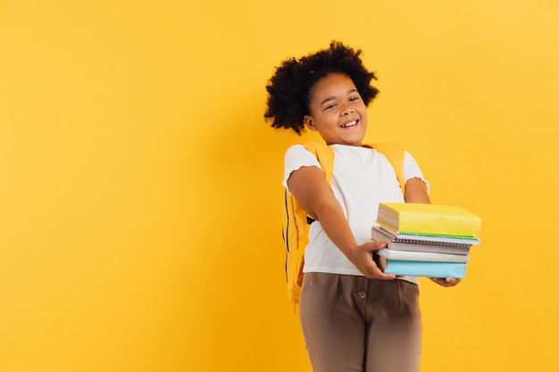 Glückliches afroamerikanisches Schulmädchen, das Notizbücher und Bücher auf gelbem Hintergrund hält, kopieren Raum