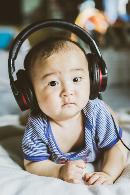 Glückliches asiatisches Baby, das Musik unter Verwendung der großen schwarzen Kopfhörer genießt.