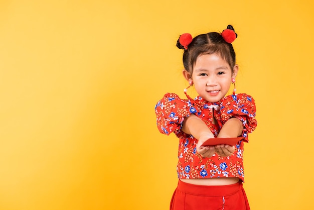 Glückliches asiatisches chinesisches kleines Mädchenlächeln tragen rotes Cheongsam überreichtes Angpao oder rotes Paket Geldgeschenk