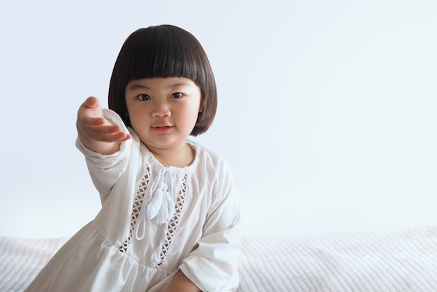 Glückliches asiatisches Kind, das auf Bett mit weißer Wand sitzt