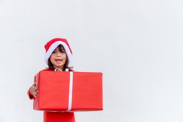 Glückliches asiatisches Kind in Santa Red Hat mit Weihnachtsgeschenken. Weihnachtszeit auf weißem Hintergrund.