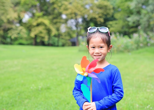 Glückliches asiatisches Kindermädchen mit Windkraftanlage im Garten