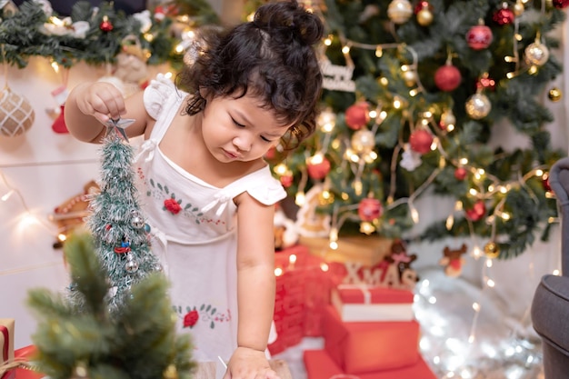 Glückliches asiatisches kleines Mädchen hat Spaß am Weihnachtstag. Kind mit Elternteil mit Weihnachtsbaumdekoration zu Hause im Urlaub.