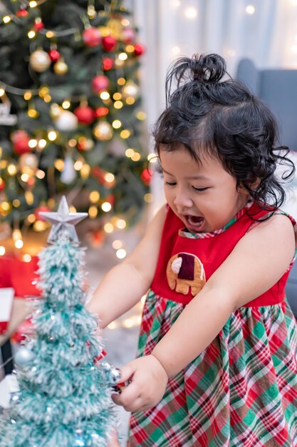 Glückliches asiatisches kleines Mädchen hat Spaß am Weihnachtstag. Kind mit Elternteil mit Weihnachtsbaumdekoration zu Hause im Urlaub.