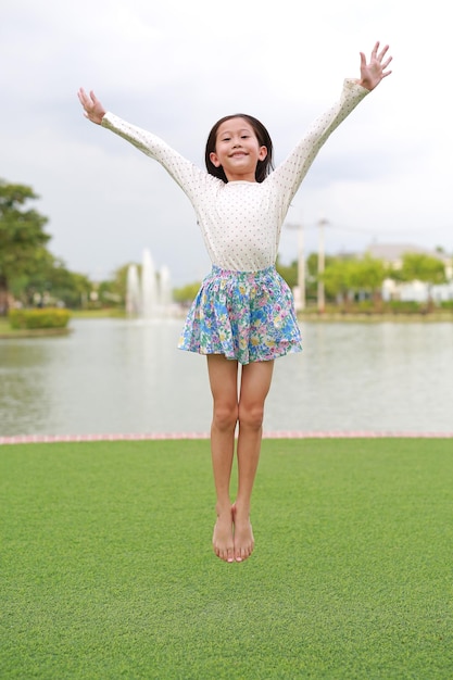 Glückliches asiatisches Mädchen, das im Garten im Freien springt