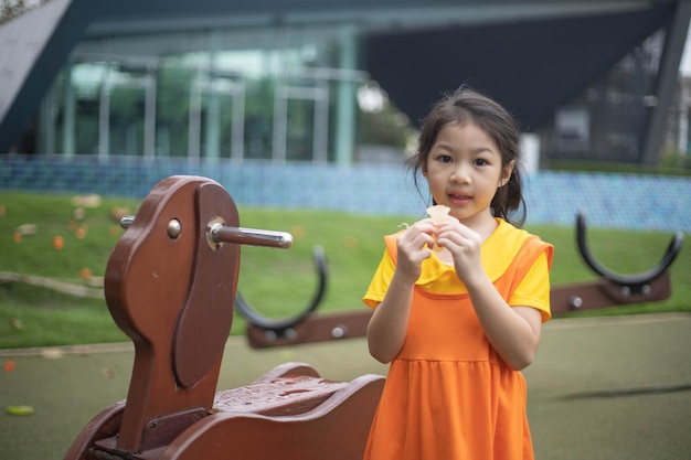 Glückliches asiatisches Mädchen im orangefarbenen Kleid, das Geleebonbons isst