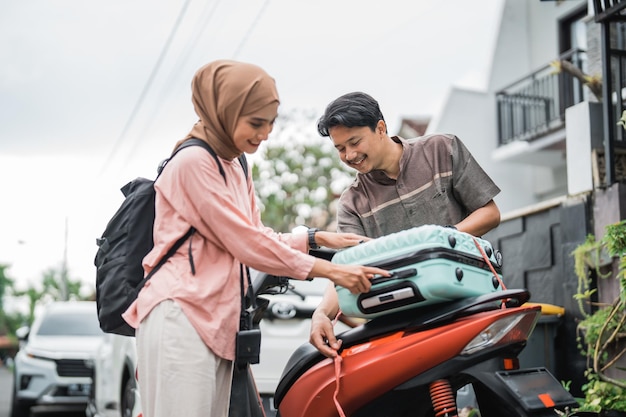 Glückliches asiatisches muslimisches paar packt seinen koffer auf motorradreisen während eid mubarak zurück in die heimatstadt