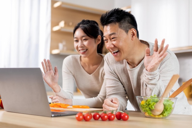 Glückliches asiatisches Paar beim Video-Chat beim Kochen in der Küche