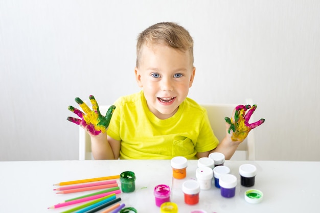 Glückliches Baby, das das Kind mit seinen Fingern mit hellen Farben zeichnet, lächelt in die Kamera