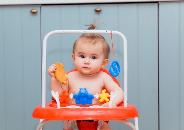 Glückliches Baby, das in roten Wanderern sitzt und einen Cracker isst. Baby lächelt