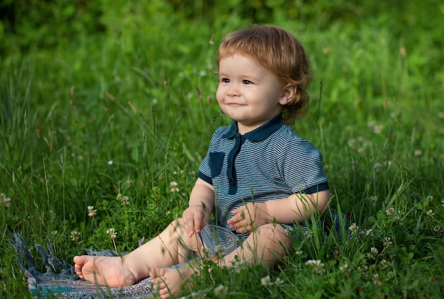 Glückliches Baby im Gras auf dem Feld am sonnigen Sommerabend Lächelndes Kind im Freien