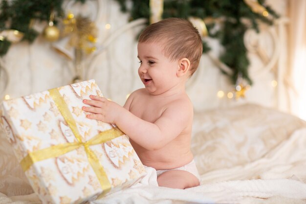 Glückliches Baby in einer Weihnachtsmütze mit einem Geschenk