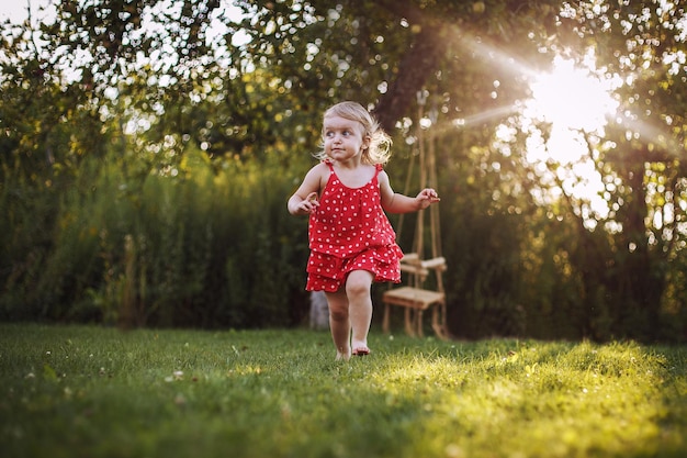 Glückliches Baby lächelndes kleines Mädchen, das bei Sonnenuntergang im Freien barfuß im Garten läuft