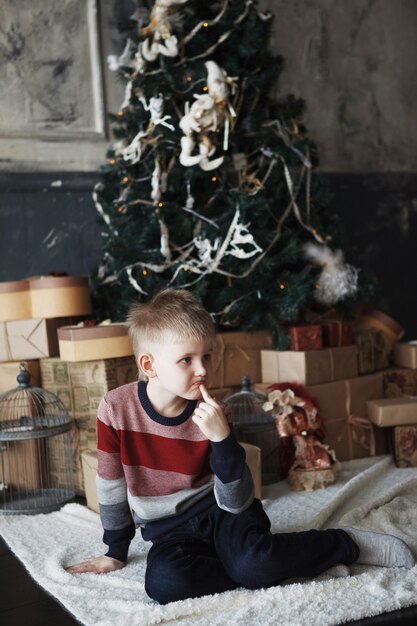 Glückliches Baby mit vielen Geschenk- und Geschenkboxen in der Nähe des geschmückten Weihnachtsbaums! Kind in roter Weihnachtsmütze gekleidet. Weihnachts- und Neujahrsferien