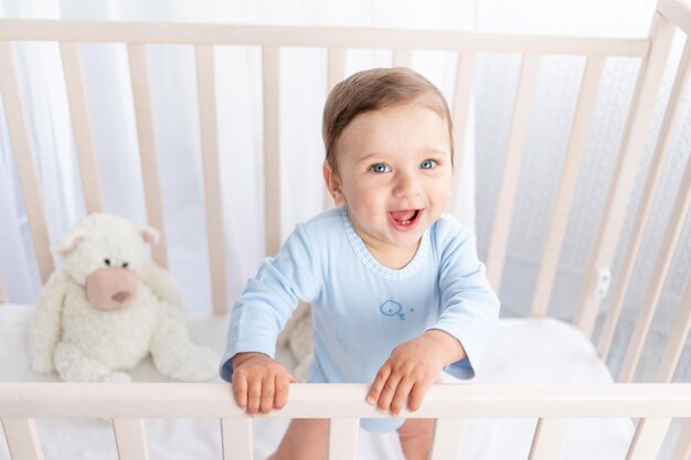 Glückliches Baby steht in der Krippe im Kinderzimmer und lächelt oder lacht