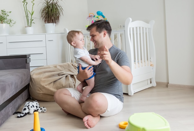 Glückliches Baby und junger Vater, die im Wohnzimmer spielen