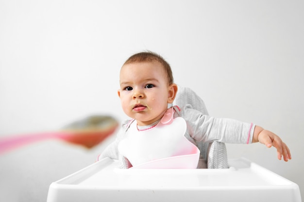 Glückliches Babykleinkind im Hochstuhl mit Löffel in seiner Hand