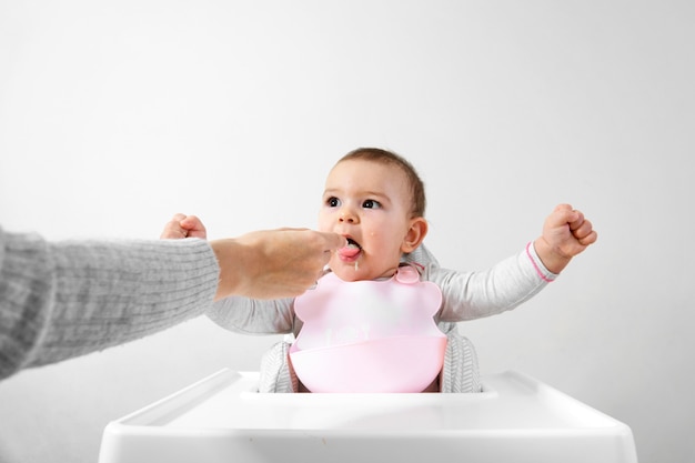 Glückliches Babykleinkind im Hochstuhl mit Löffel in seiner Hand