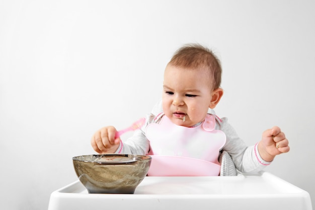 Glückliches Babykleinkind im Hochstuhl mit Löffel in seiner Hand