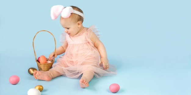 Glückliches Babymädchen auf blauem Studiohintergrund und spielen mit farbigen Ostereiern Kleines Osterkind